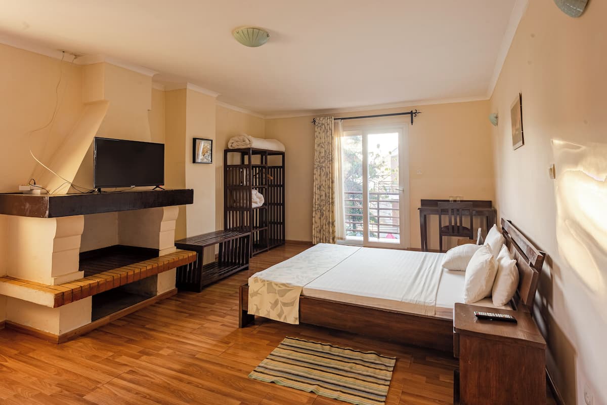 Un dormitorio con cama de madera, televisor en un mueble, una mesita y un balcón con vistas.
