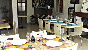 Un comedor con una mesa larga dispuesta para seis personas, rodeada de sillas. Se observa una cocina con un refrigerador y un microondas al fondo.