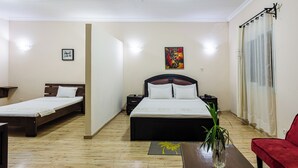 Habitación de hotel con dos camas individuales, un sofá rojo, una mesa de centro de madera, una planta y un cuadro en la pared.
