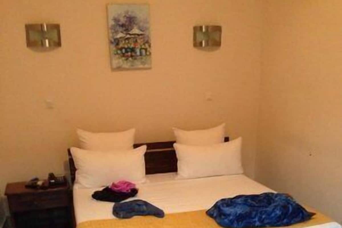 Een slaapkamer met een bed, kussens, een nachtkastje en een vloerkleed.