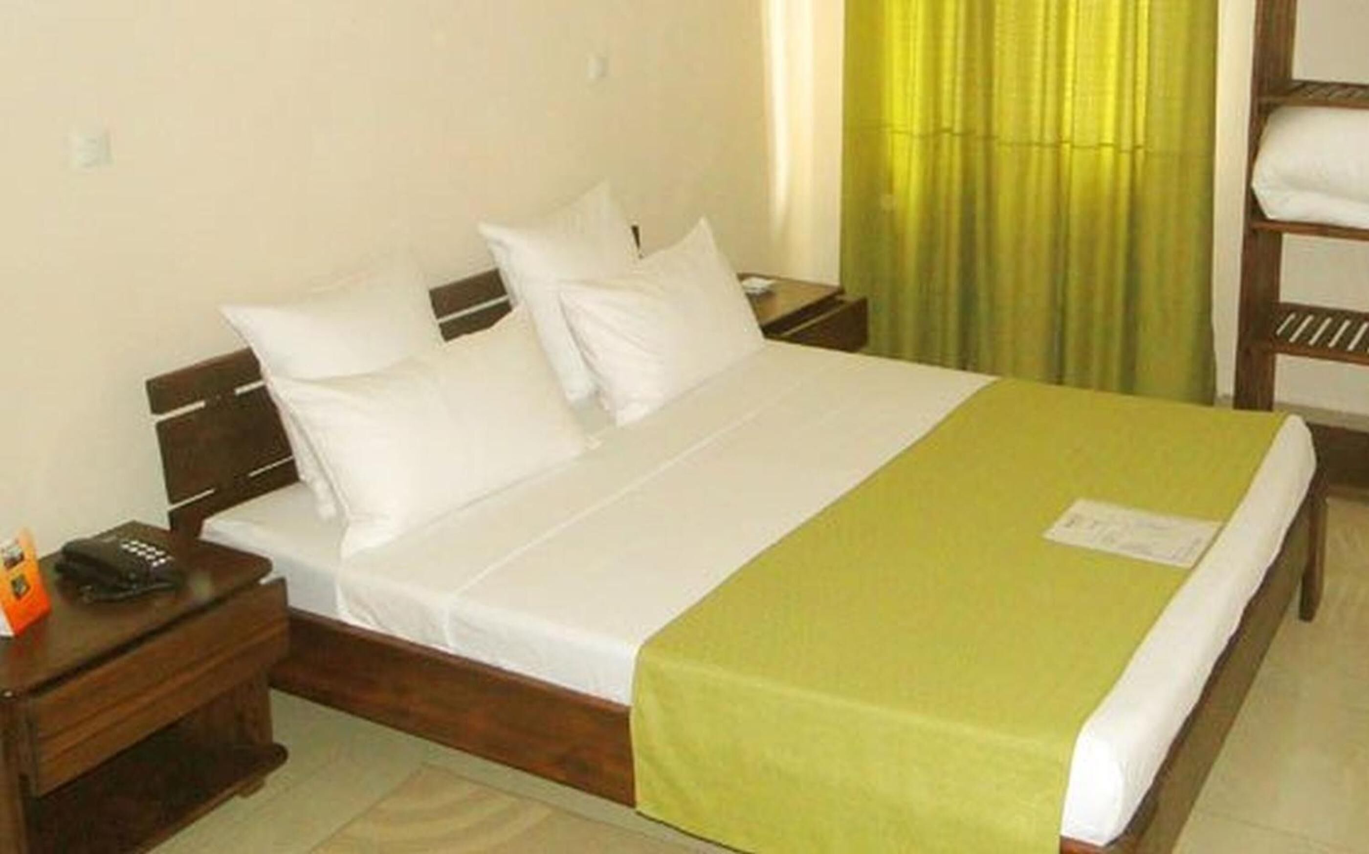 A neatly made bed with white linens and a green bedspread in a hotel room.