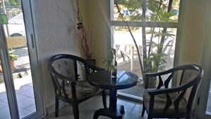 Et værelse med en glasdør, der fører ud, to stole, et rundt bord og en potteplante.