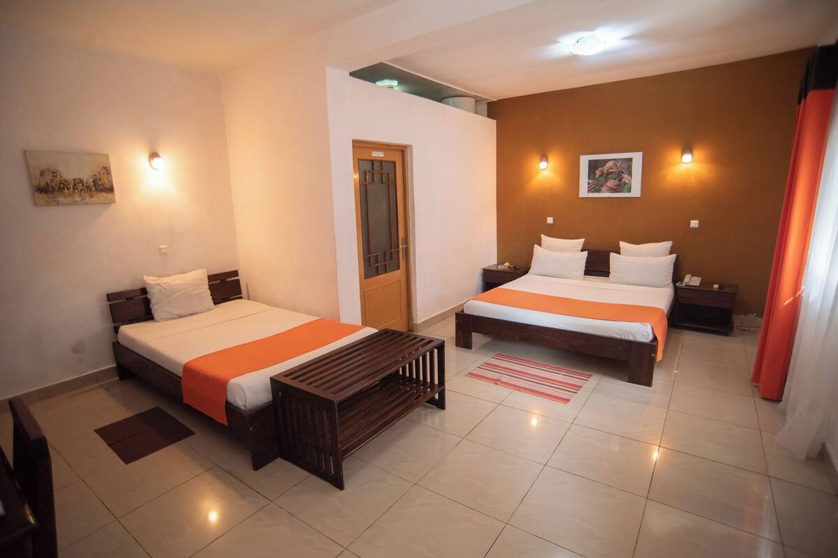 Een hotelkamer met twee bedden, een houten bankje, een klein tafeltje en een nachtkastje.