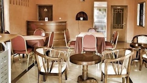 Spisested i et hotel med flere borde og stole, en reception og et flisegulv.