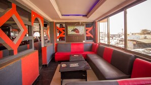A modern interior with red and grey seating, a TV screen, and large windows offering a city view. - Hotel Nomad (Kitengela)