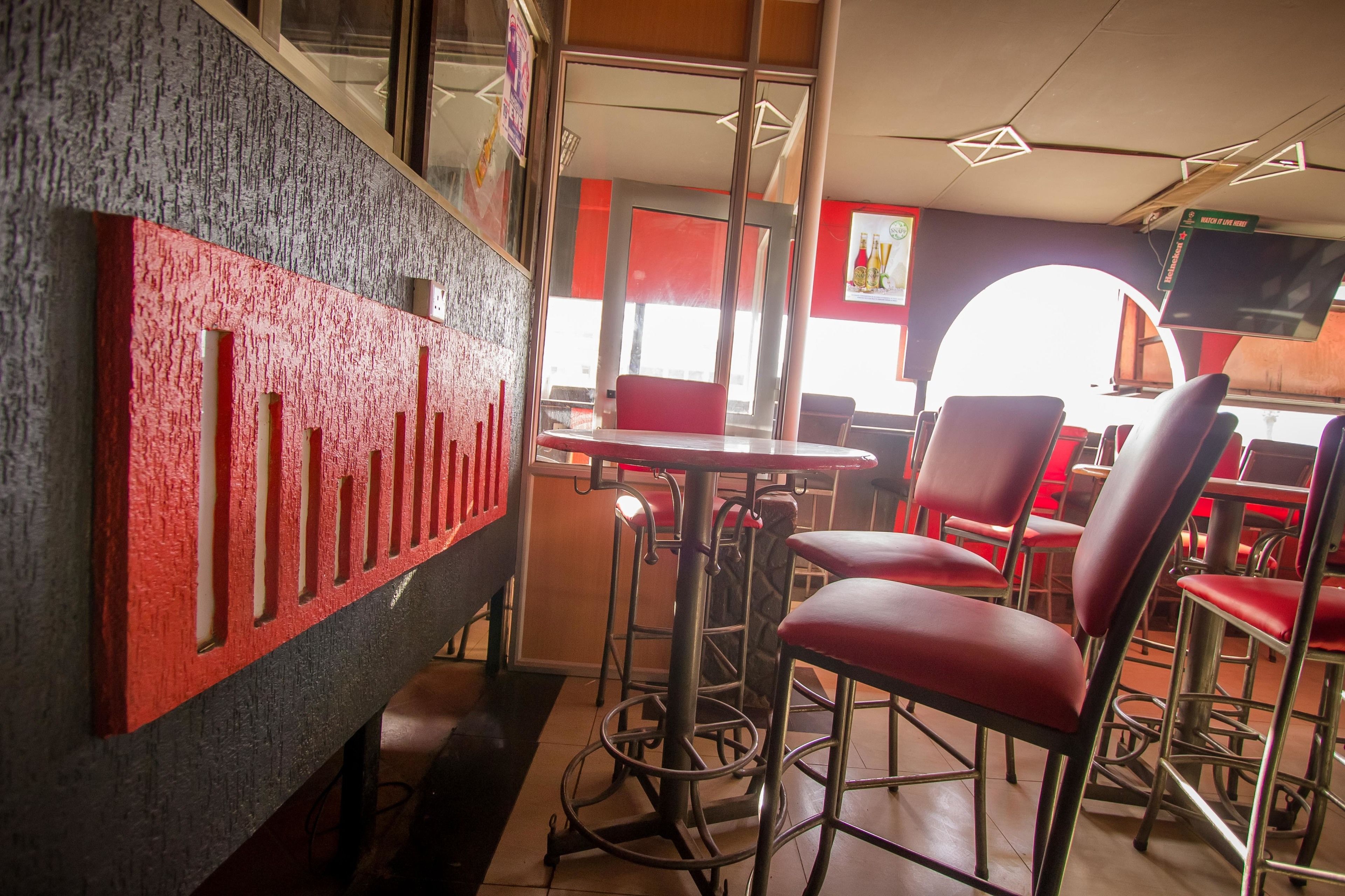 Interior de restaurante con taburetes altos, sillas rojas y una barra.