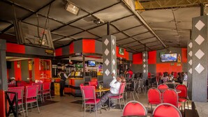 A restaurant with red and grey decor, multiple tables and chairs, and a bar area. - Hotel Nomad (Kitengela)