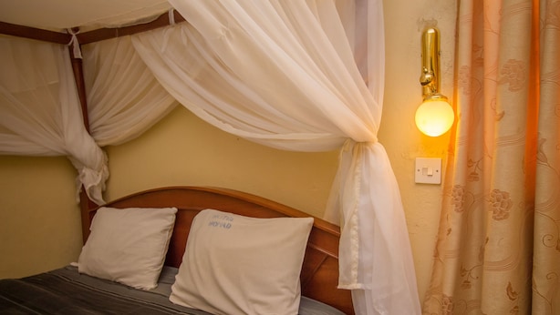 A bed with a canopy, a wall-mounted light, and a power outlet. - Hotel Nomad (Kitengela)