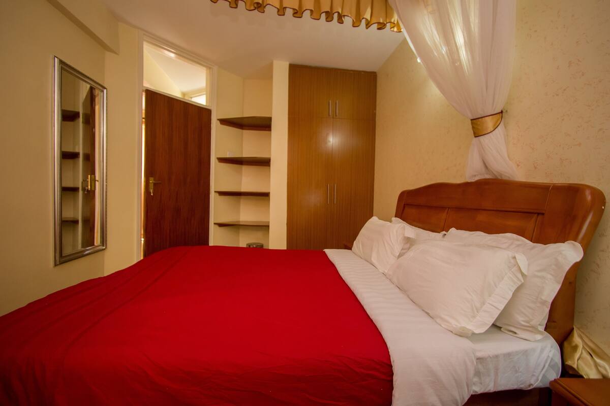 Une chambre à coucher avec une tête de lit en bois, une couvre-lit rouge, des oreillers blancs et un baldaquin.