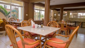 Un restaurant avec des chaises en osier et des coussins rouges, de grandes fenêtres et un sol carrelé.