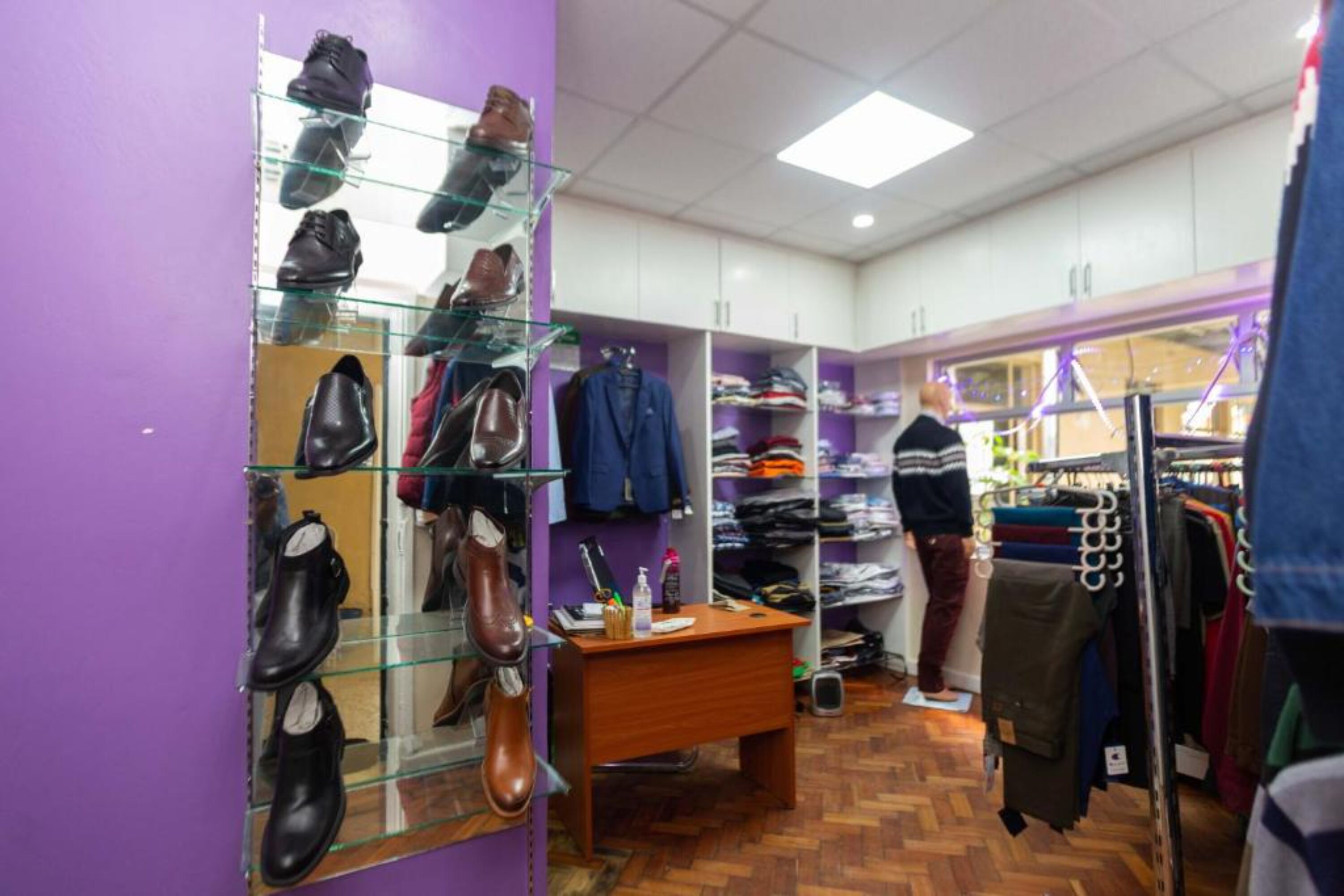 Un magasin de chaussures avec des vitrines en verre, un bureau en bois et des étagères remplies de vêtements.