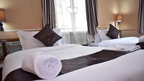 A hotel room with two beds, each with white linens and brown pillows. There is a rolled towel on the bed in the foreground. - Impala Hotel (Nairobi)