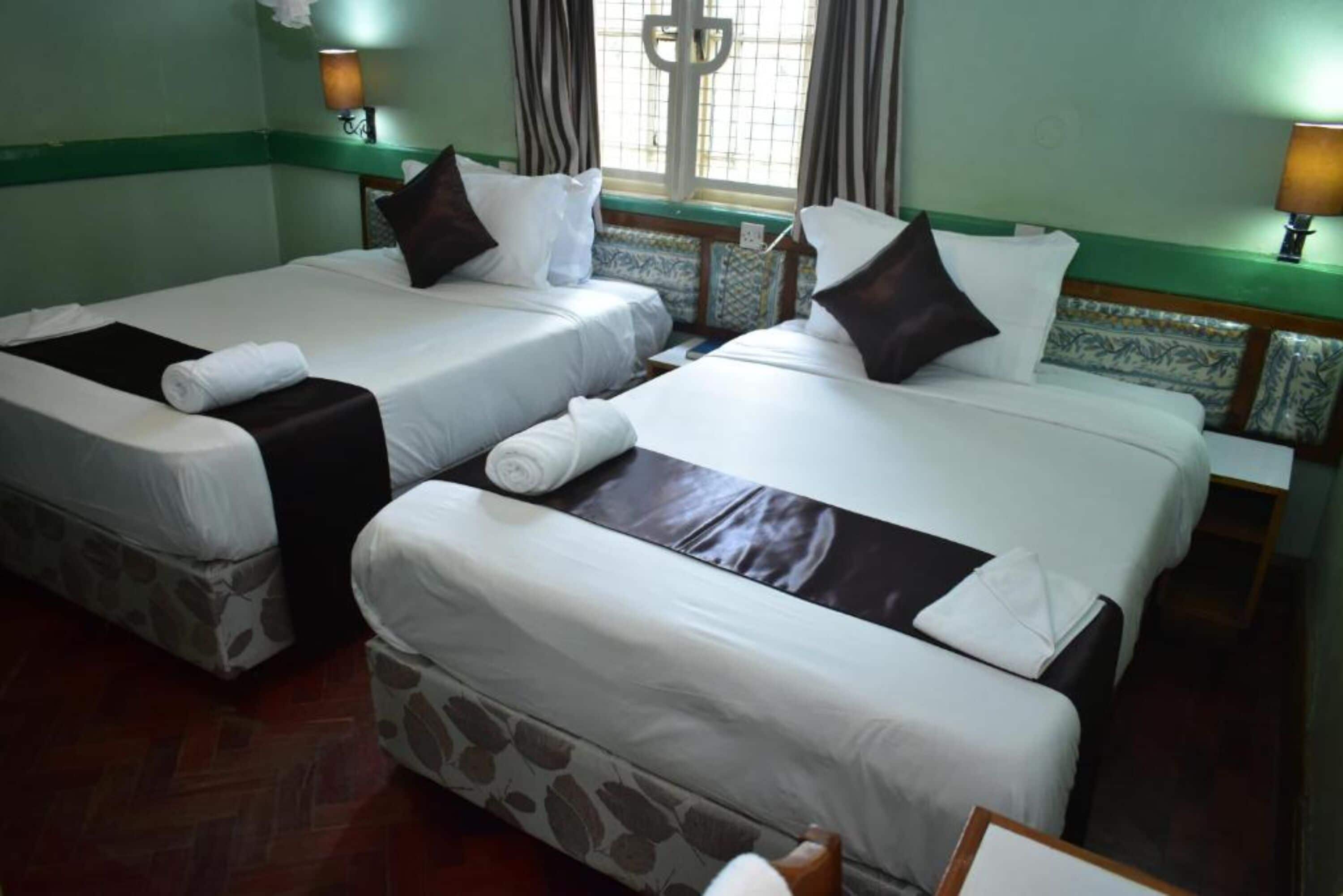 Una habitación de hotel con dos camas individuales, cada una con una almohada y una toalla enrollada.