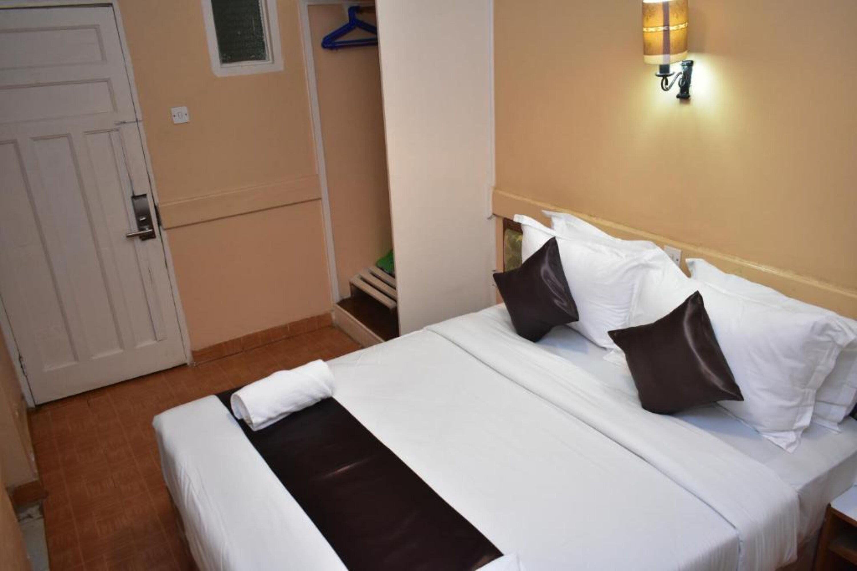 Una cama bien hecha con almohadas blancas y oscuras, una colcha blanca y un detalle en tono marrón.