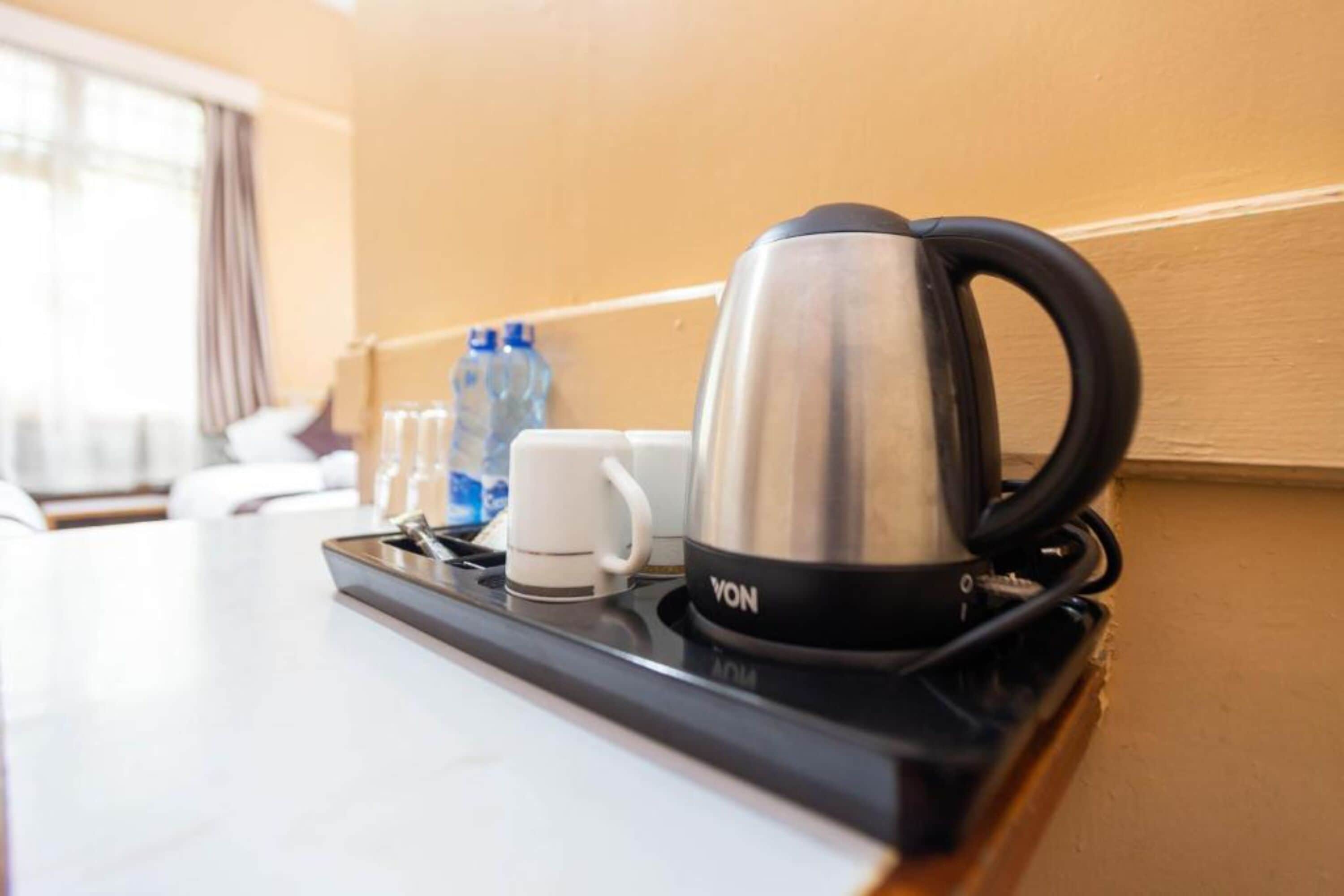 Una encimera de cocina con un hervidor de acero inoxidable, una taza blanca y una botella de agua.