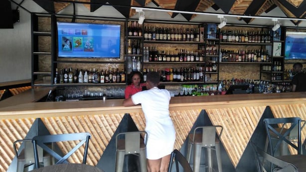 A bar area with a wooden ceiling, shelves stocked with bottles, and a television screen. - Impala Hotel (Nairobi)
