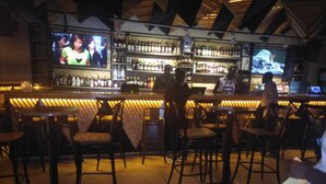 A bar area with multiple seating arrangements, a television screen, and shelves stocked with bottles. - Impala Hotel (Nairobi)