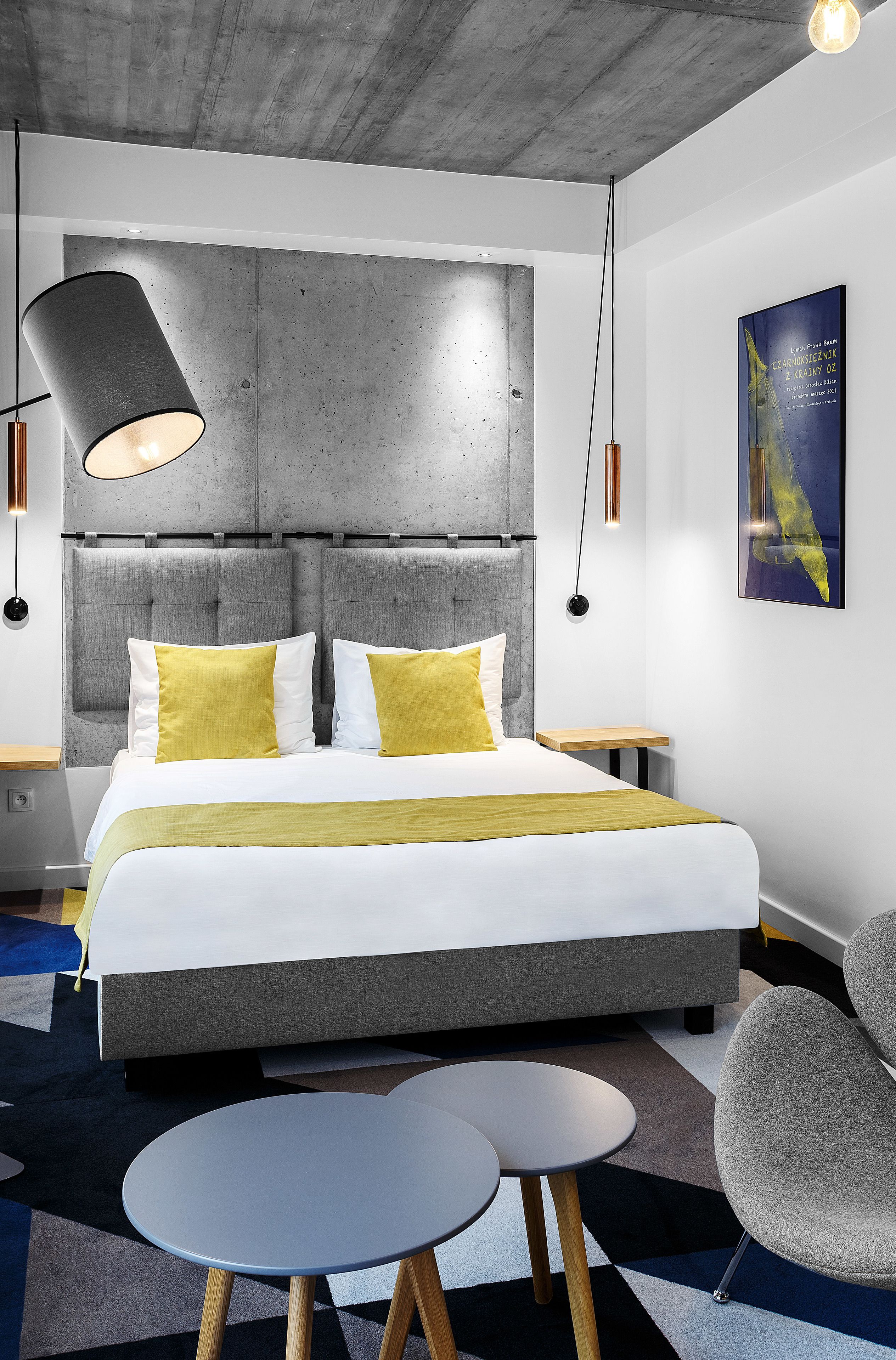 A modern hotel room with a large bed, a round table, and a gray armchair.