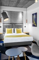 Una habitación de hotel moderna con una cama grande, una mesa redonda y un sillón gris.