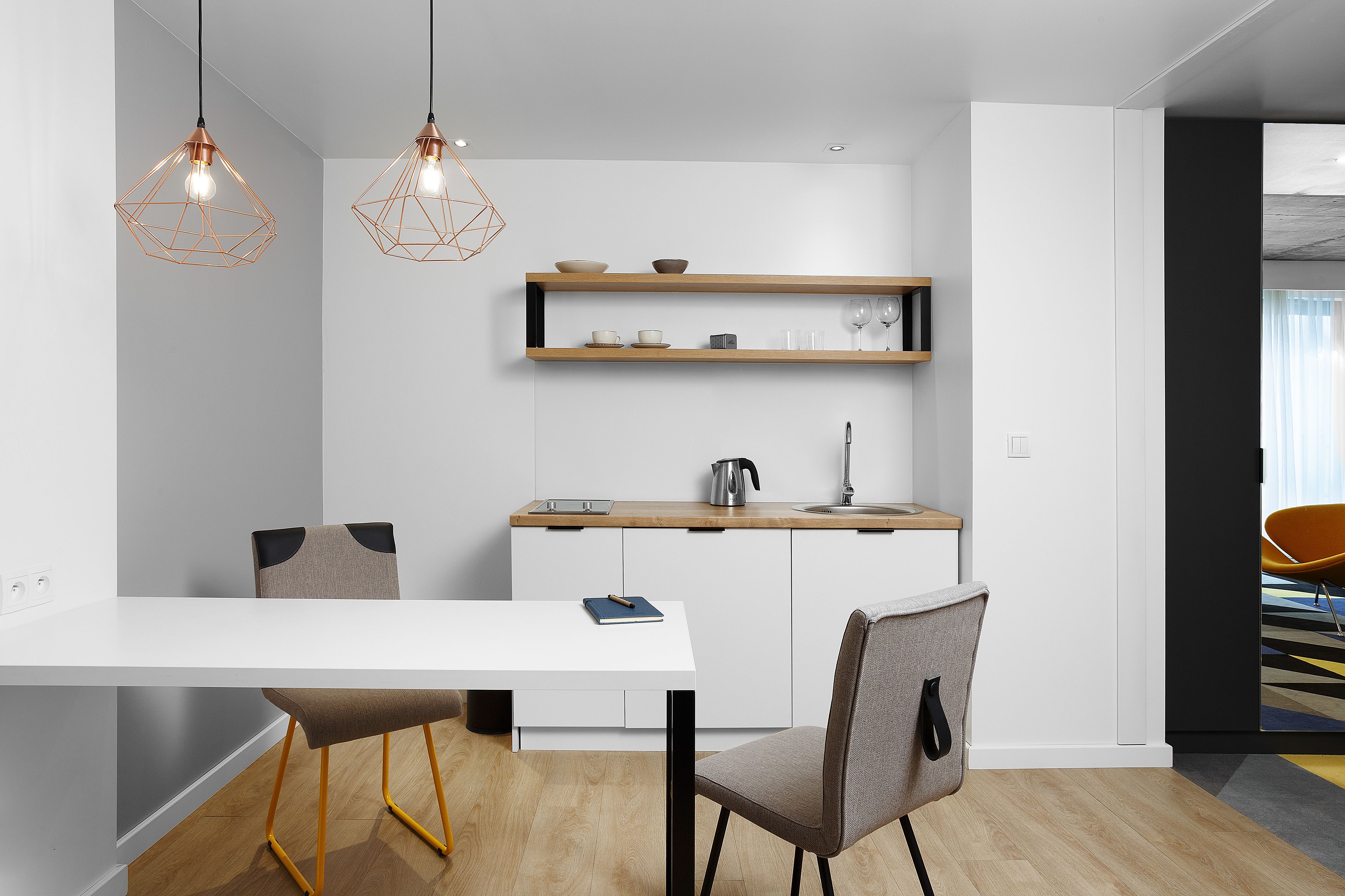 A modern kitchen with white cabinetry, a wooden countertop, and pendant lighting. There is a dining table with chairs, a coffee machine, and a kettle on the counter.