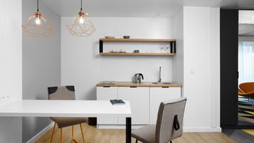 A modern kitchen with white cabinetry, a wooden countertop, and pendant lighting. There is a dining table with chairs, a coffee machine, and a kettle on the counter.
