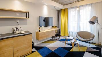 Una habitación de hotel moderna con un armario de madera, un televisor de pantalla plana, una mesita, una silla y una alfombra estampada.