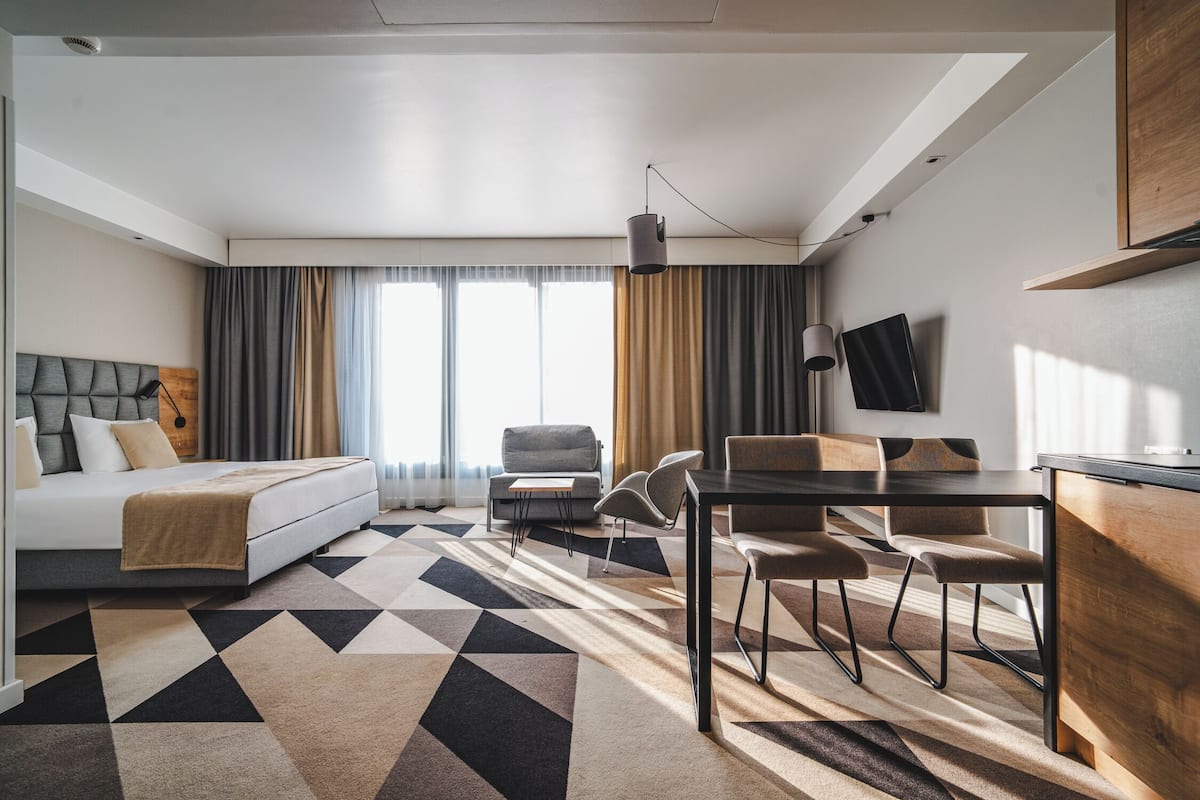 Moderni hotellihuone, jossa on sänky, ruokailutila ja seinälle asennettu televisio.