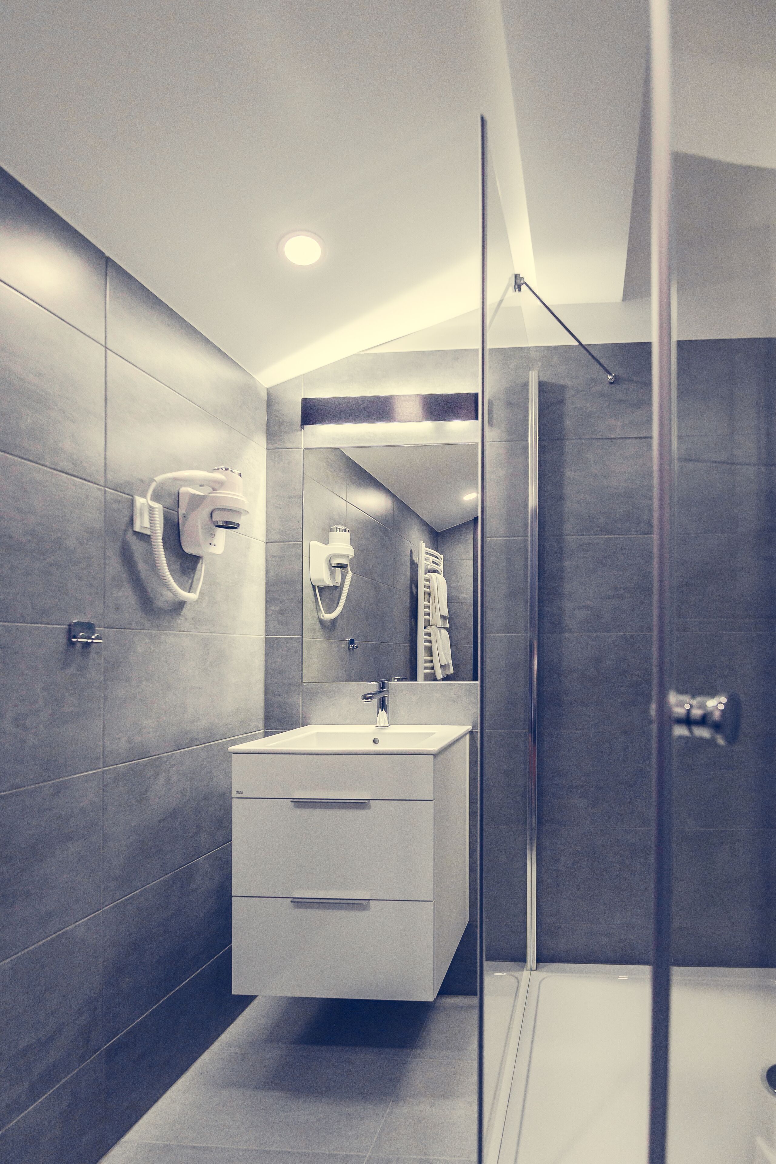 A modern bathroom with a glass shower enclosure, a white sink, and a towel rack.