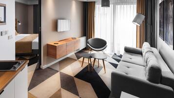 Una habitación de hotel moderna con un sofá, una silla, una mesita, un televisor montado en la pared y un armario de madera.