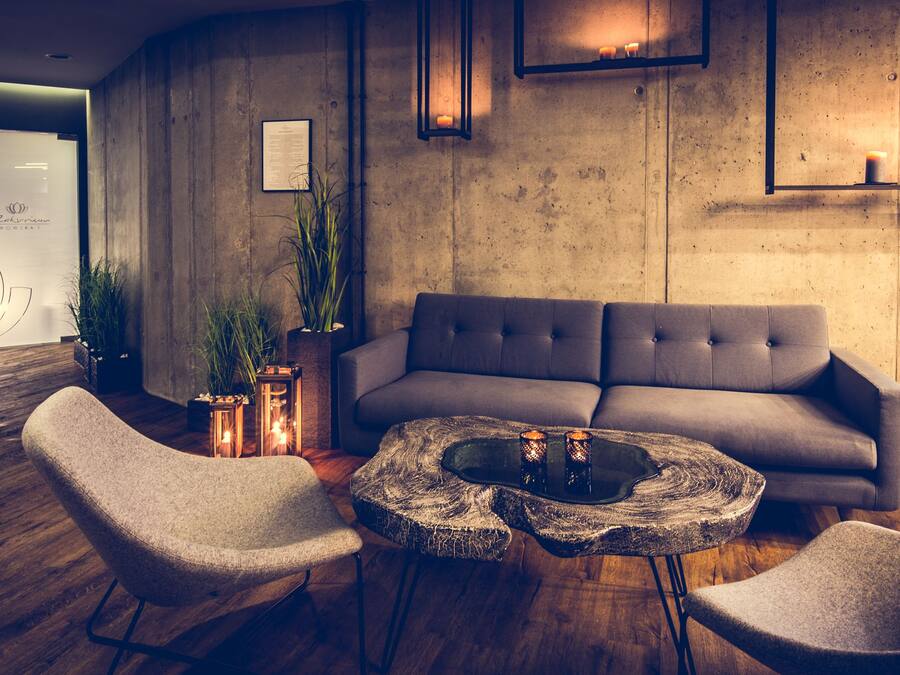 Et moderne loungeområde med en grå sofa, to lænestole, et sofabord og en vægmonteret hylde med stearinlys.