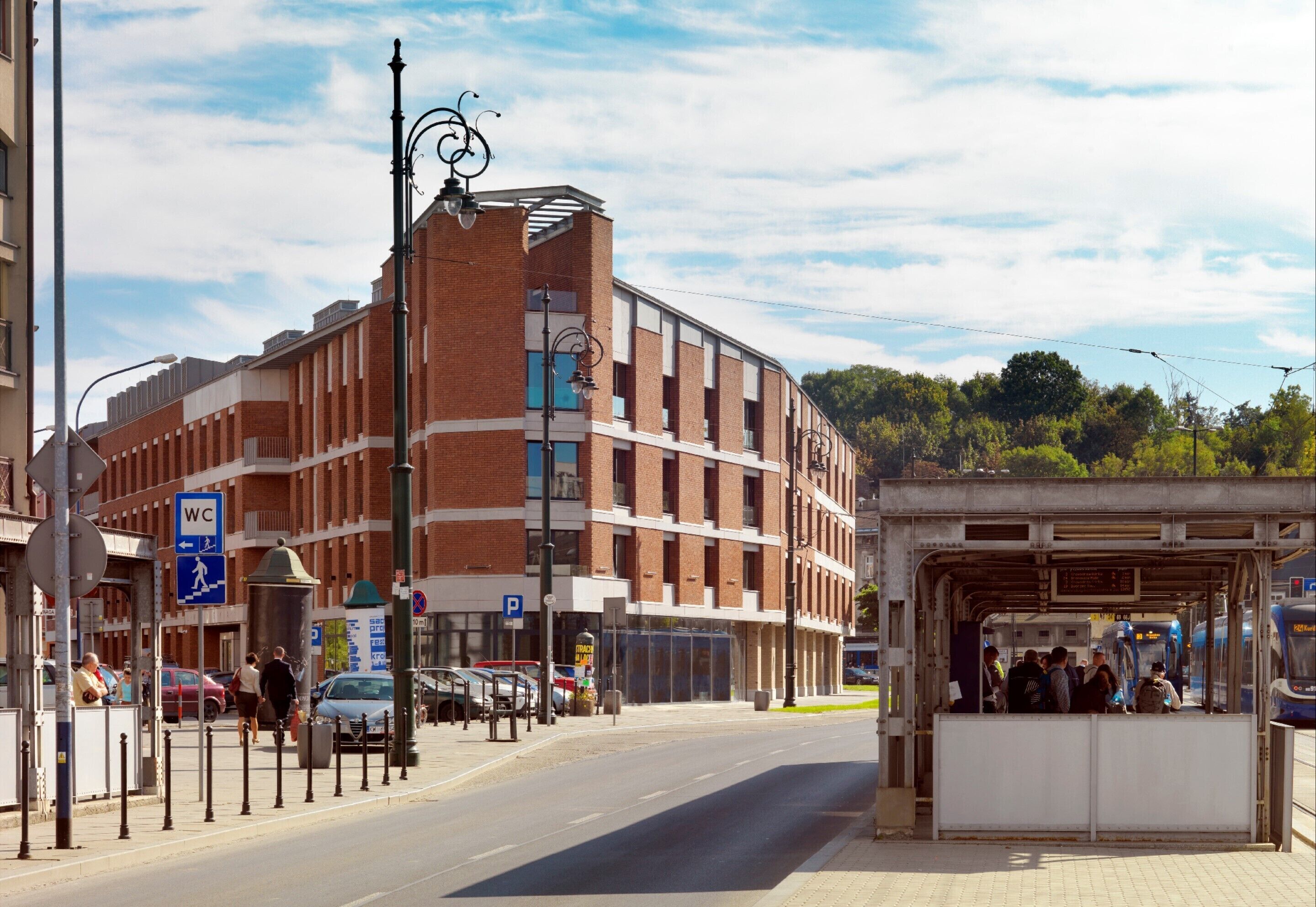 A train station platform with a covered waiting area, a pedestrian crossing, and a building with a 'WC' sign.