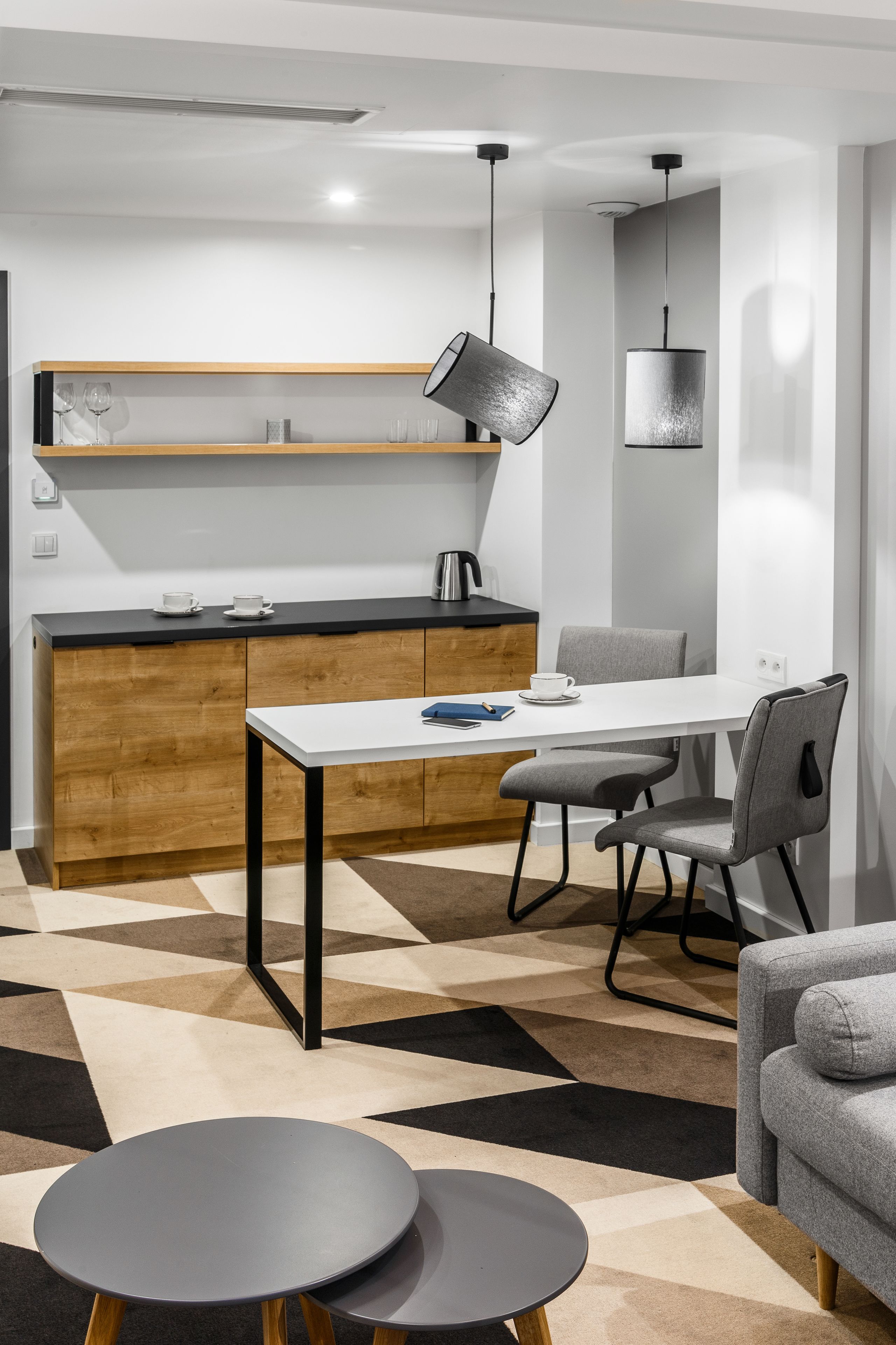 Een moderne keuken met een wit aanrecht, houten kastjes en een eethoek met een witte tafel en grijze stoelen.
