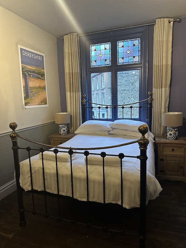 Quarto com cama de dossel, um cartaz de Derbyshire na parede e vista de um edifício de pedra pela janela.