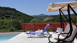 A poolside area with two lounge chairs, one with a canopy, and a red wooden fence in the background. - Villa Jazz Rock (Corfu)