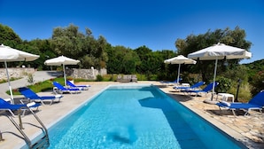 A rectangular swimming pool with clear blue water, surrounded by blue lounge chairs and white umbrellas. - Villa Jazz Rock (Corfu)