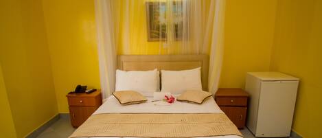 A hotel room with a bed, bedside tables, a small refrigerator, and a curtain.
