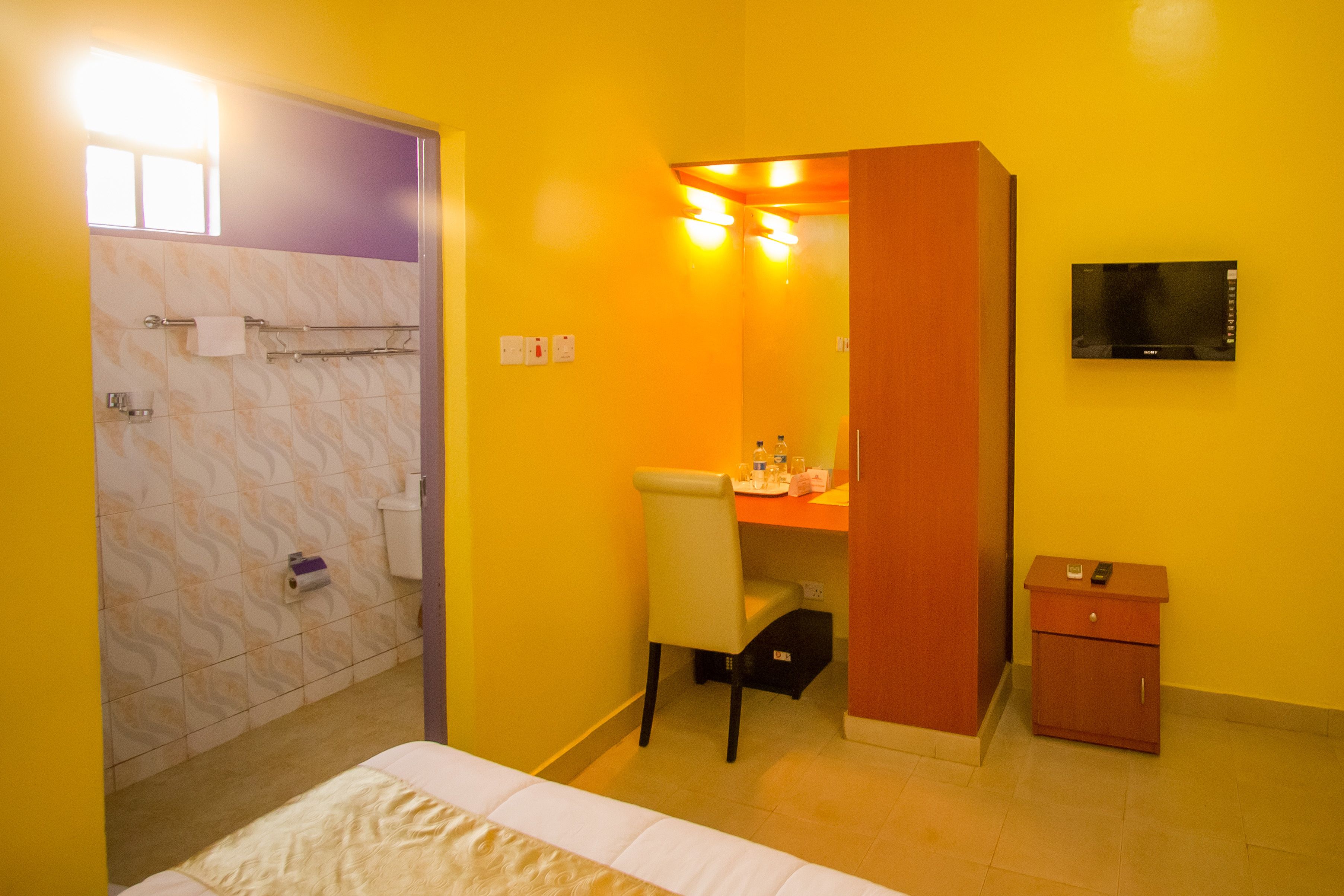 A hotel room with a bed, a desk, a chair, a small cabinet, a television, and a bathroom with a shower and toilet.