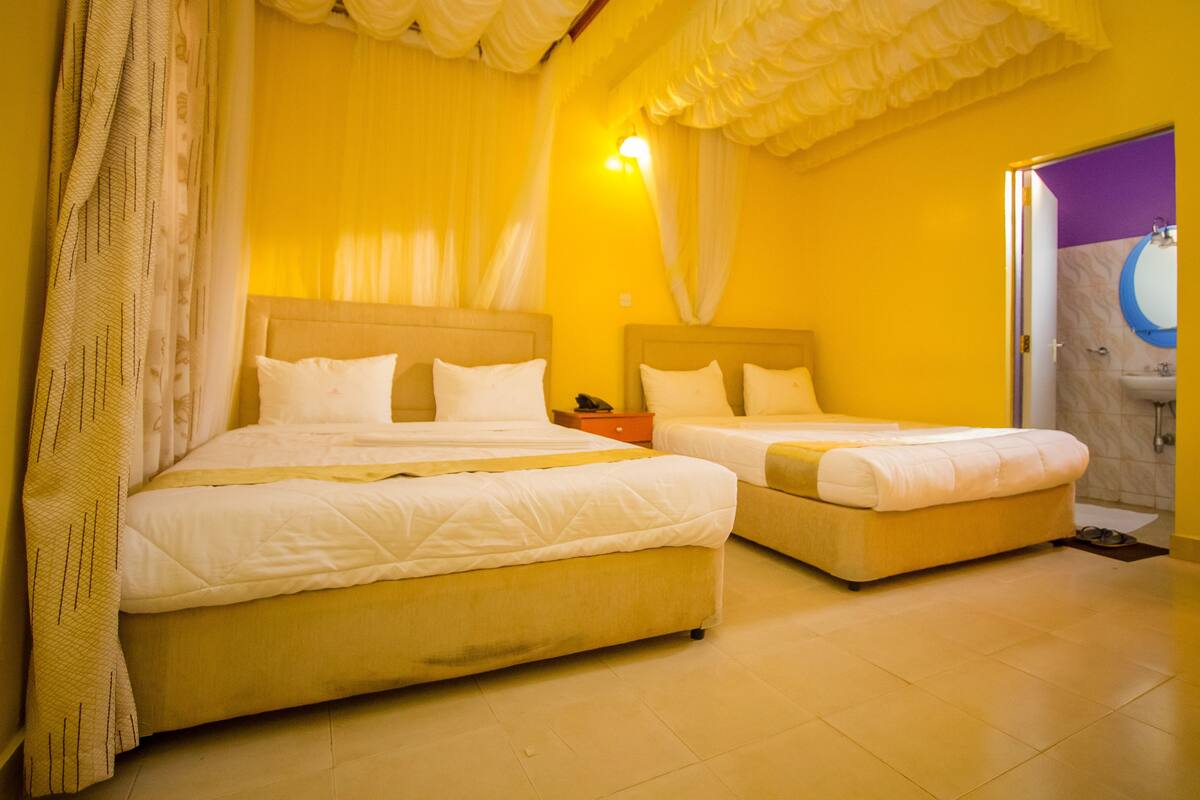 Quarto de hotel com duas camas, banheiro com parede de destaque roxa e área de chuveiro.