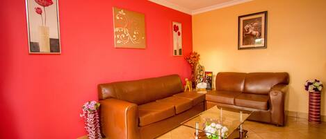 A living room with two brown leather sofas, a glass coffee table, and red walls.