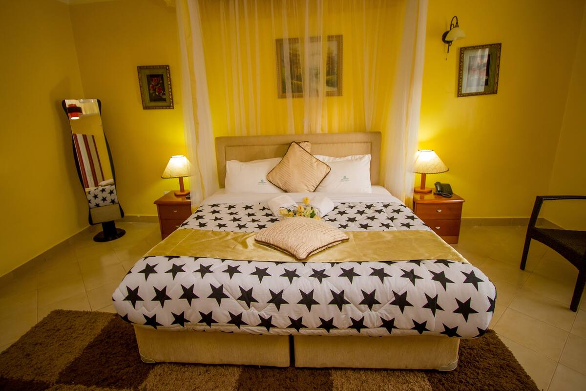 Quarto de hotel com cama coberta por um edredom estampado com padrão de estrelas, duas luminárias de cabeceira, mesa de cabeceira com luminária, espelho e uma cadeira.