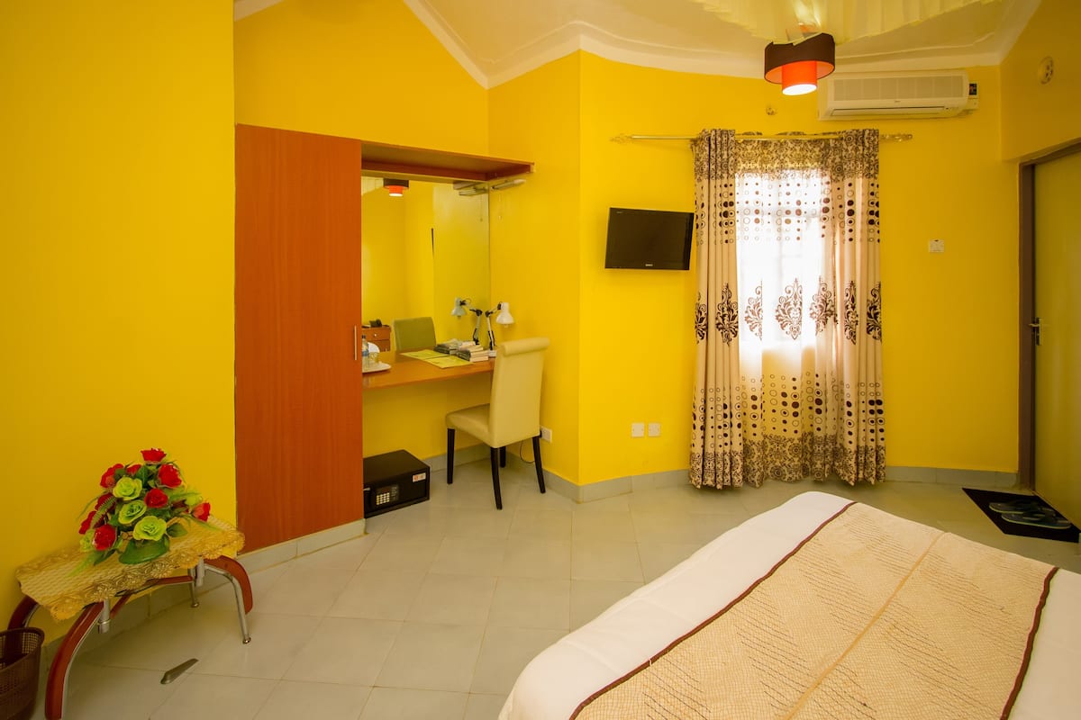 Quarto com cama, escrivaninha, cadeira e televisão.