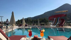 A poolside area with lounge chairs, a water slide, and a mountain in the background.