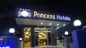 The exterior of Princess Hotels with a well-lit entrance, a reception area visible inside, and a modern architectural design with marble flooring and spherical light fixtures.