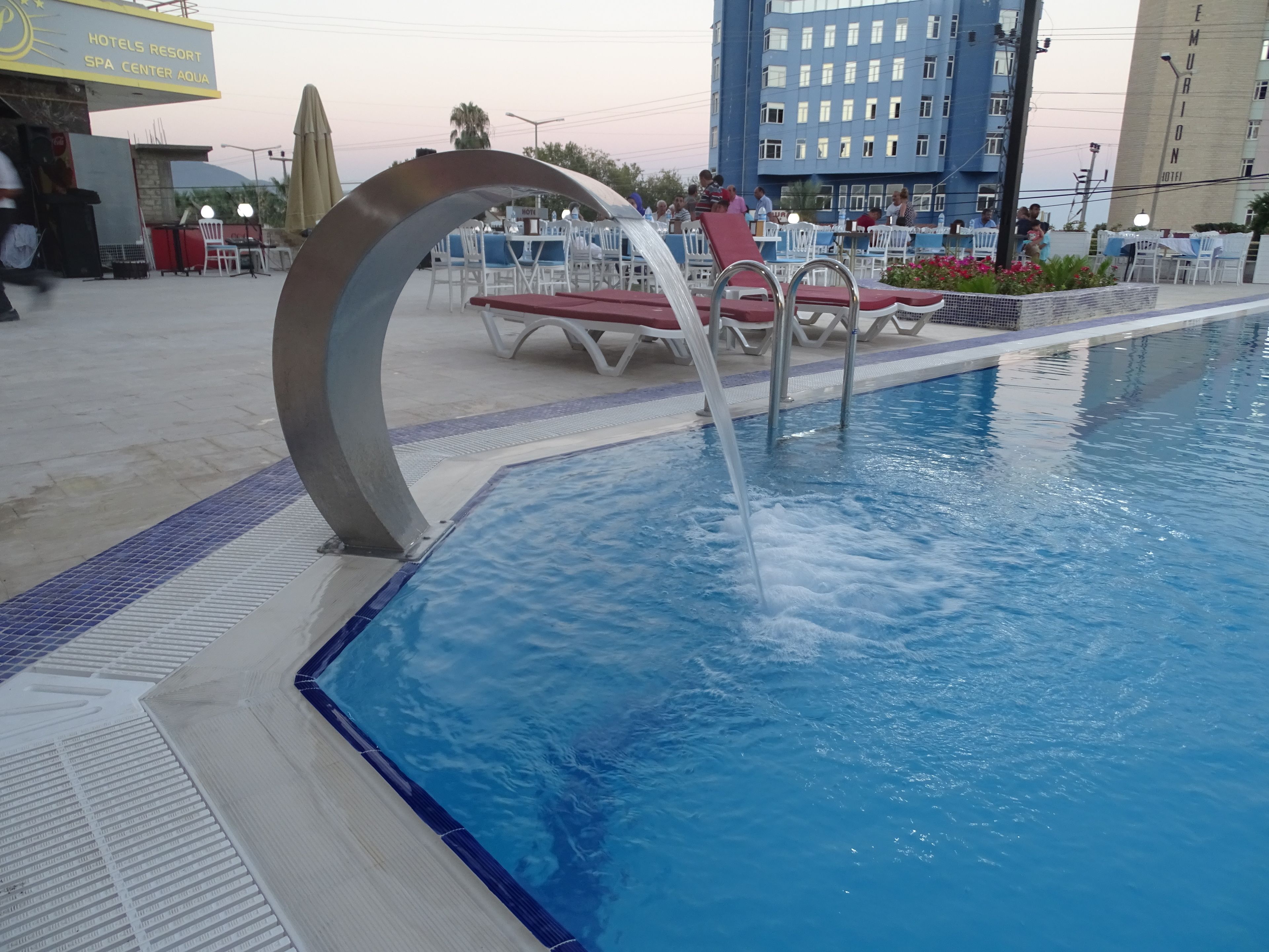 Ein Schwimmbad mit Wasserspiel, umgeben von Liegestühlen und einem Wellnessbereich.