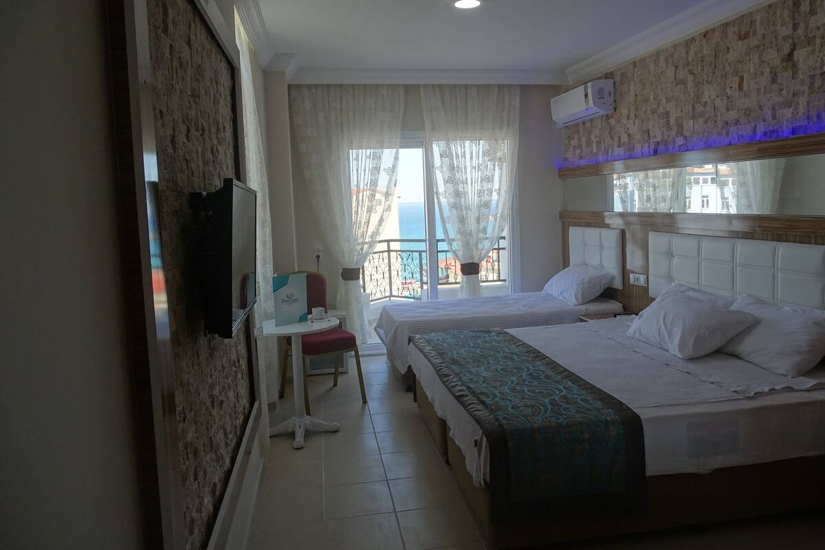 A hotel room with two beds, a desk, a TV, and a balcony with a view.