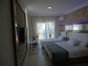 A hotel room with two beds, a desk, a TV, and a balcony with a view. - Princess Resort Hotels (Bozyazi)