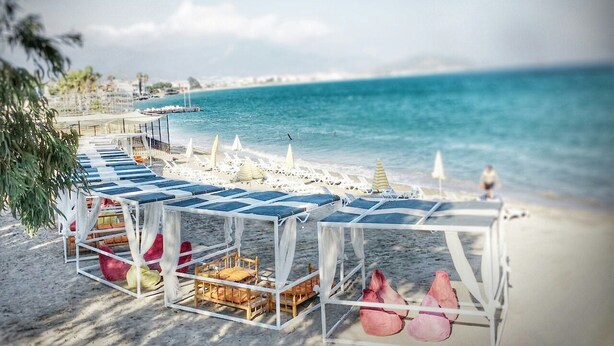 A beachside setup with sun loungers and umbrellas, a wooden deck, and a view of the sea.