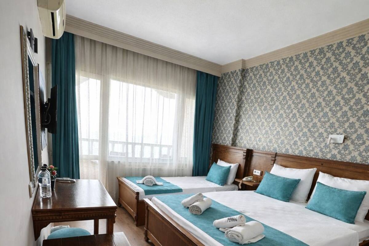 A hotel room with two beds, a desk, a TV, and a window with curtains.