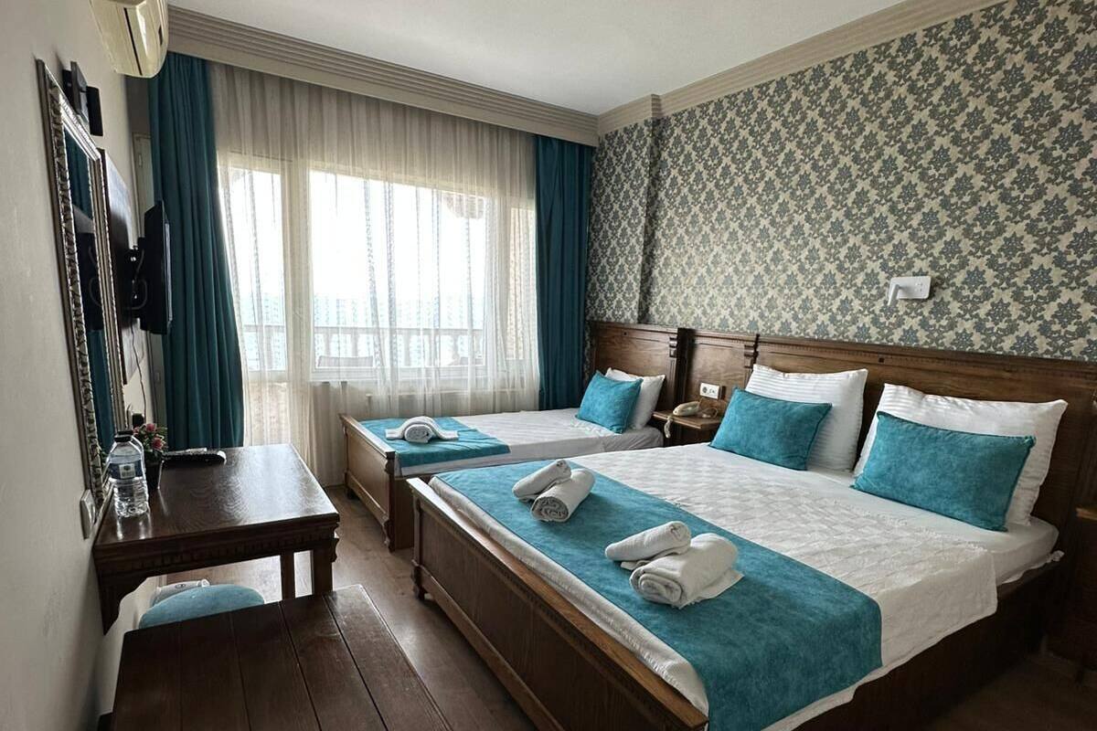 A hotel room with a bed, a desk, a chair, a window with curtains, and a patterned wall.
