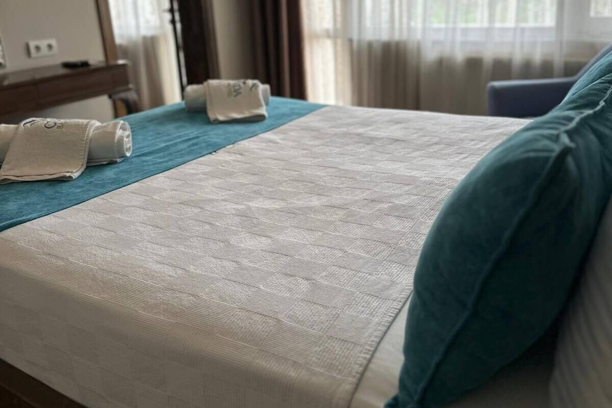 A hotel room with a bed, a bedside table, a mirror, and a window with curtains.